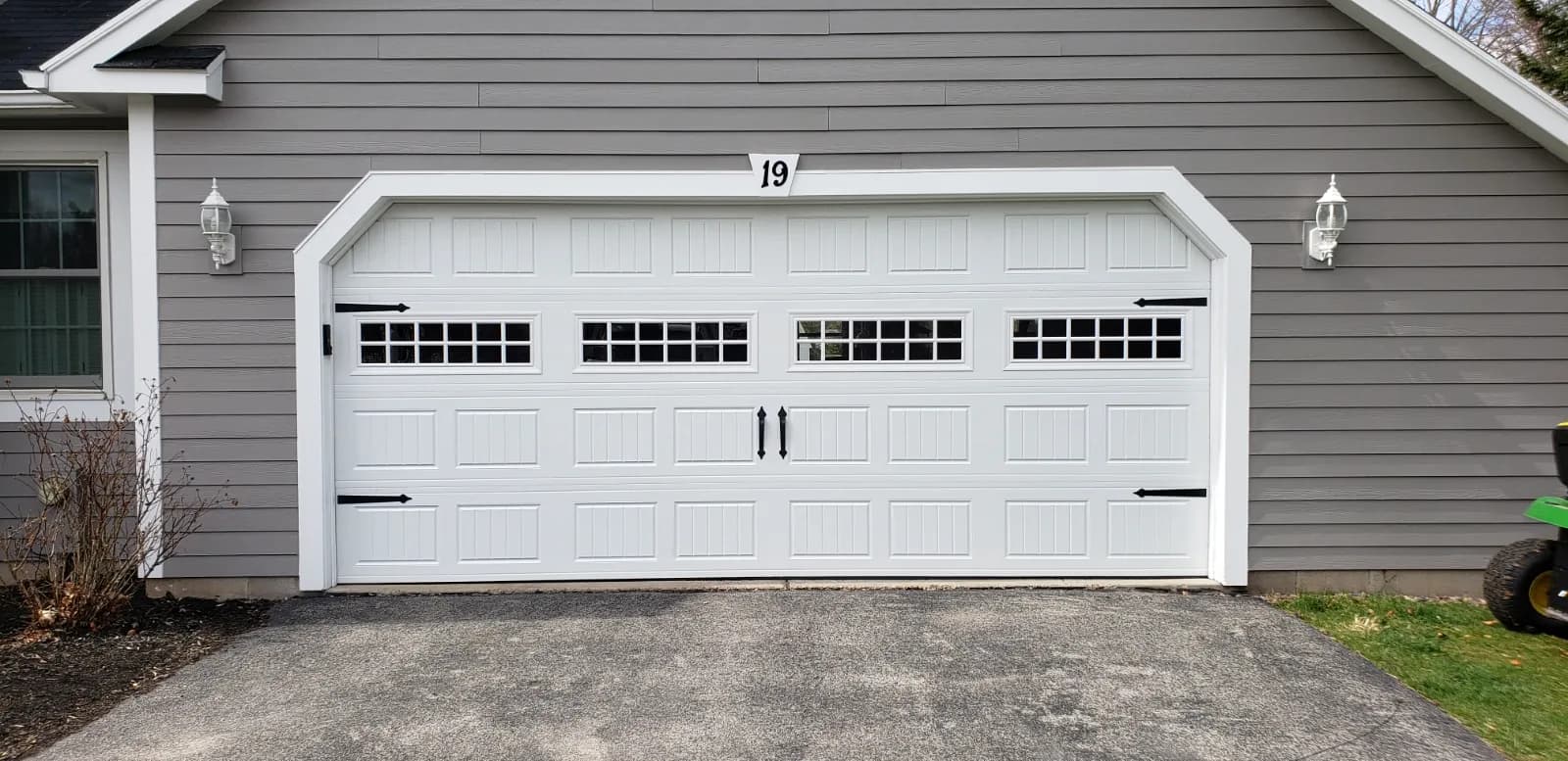 White carriage house garage door with grid windows and decorative hardware on a gray-sided home