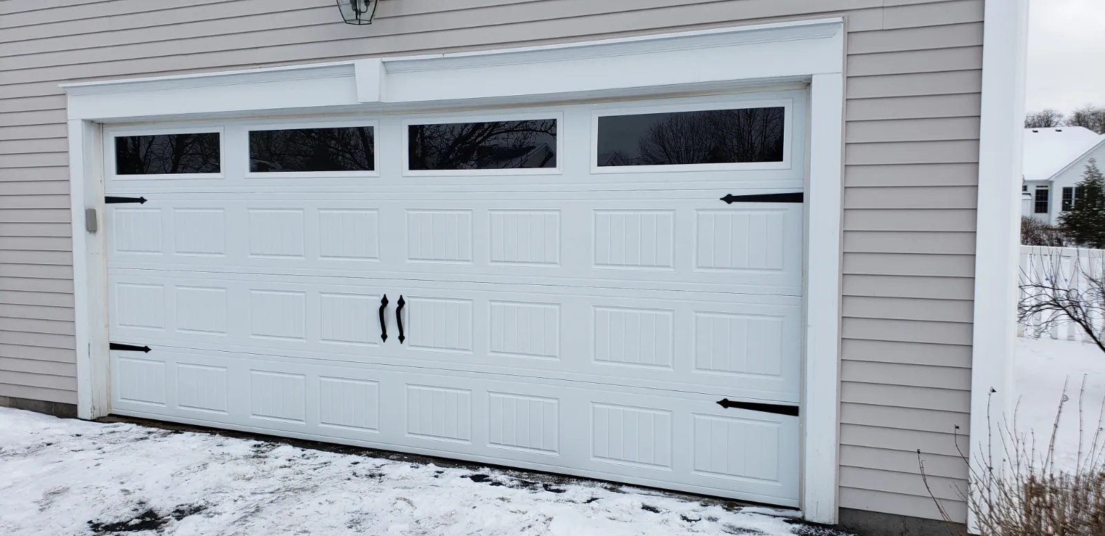 White carriage house garage door with plain windows and decorative hardware installed in winter