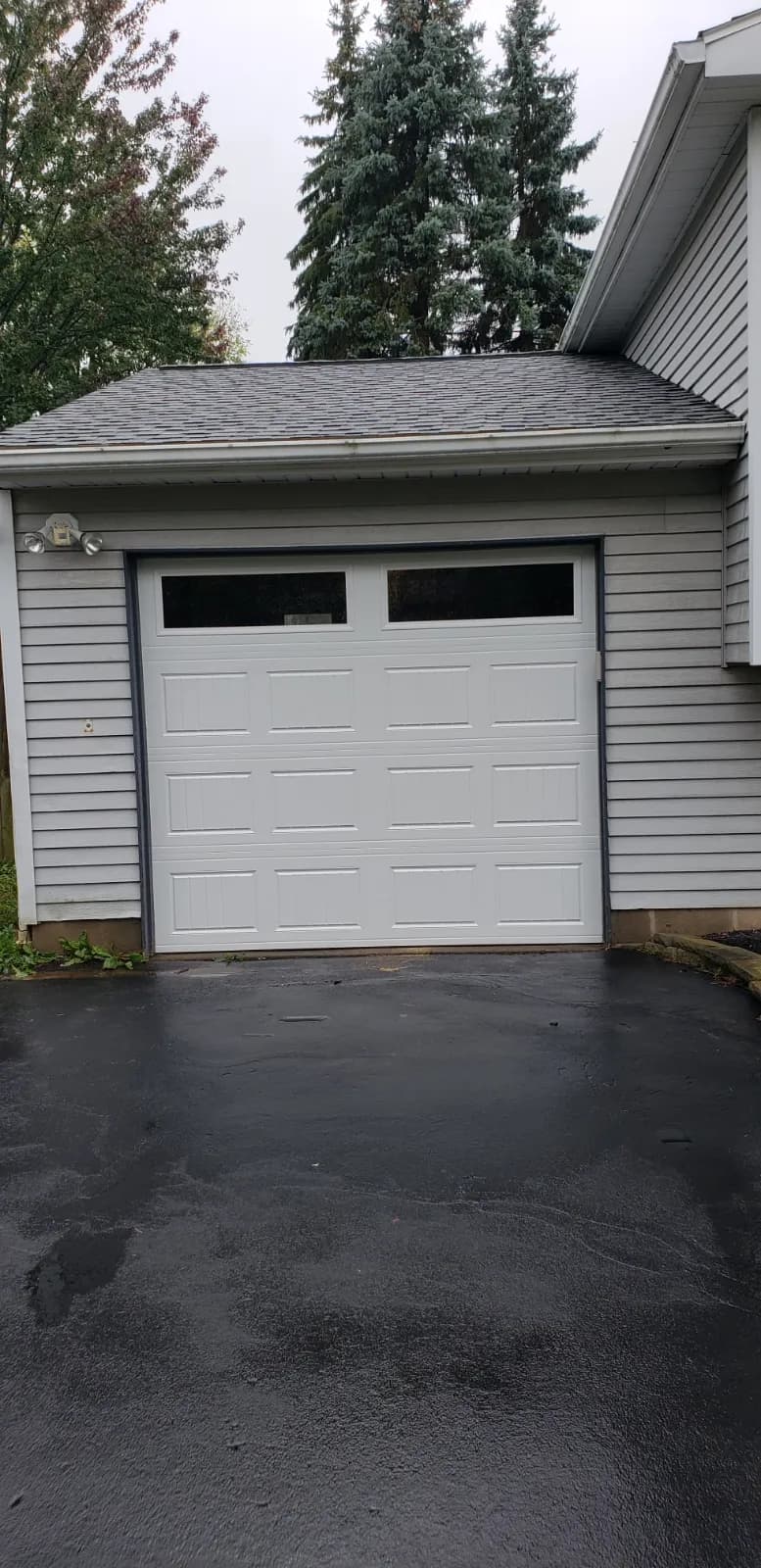 White raised panel single-car garage door with windows on a gray-sided home