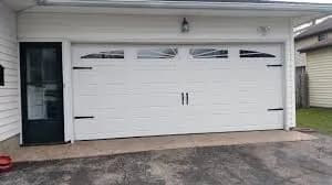 White carriage house garage door with arched windows and decorative hardware