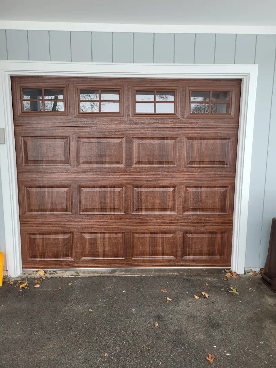 Walnut woodgrain garage door with transom windows on a home with blue-gray board-and-batten siding