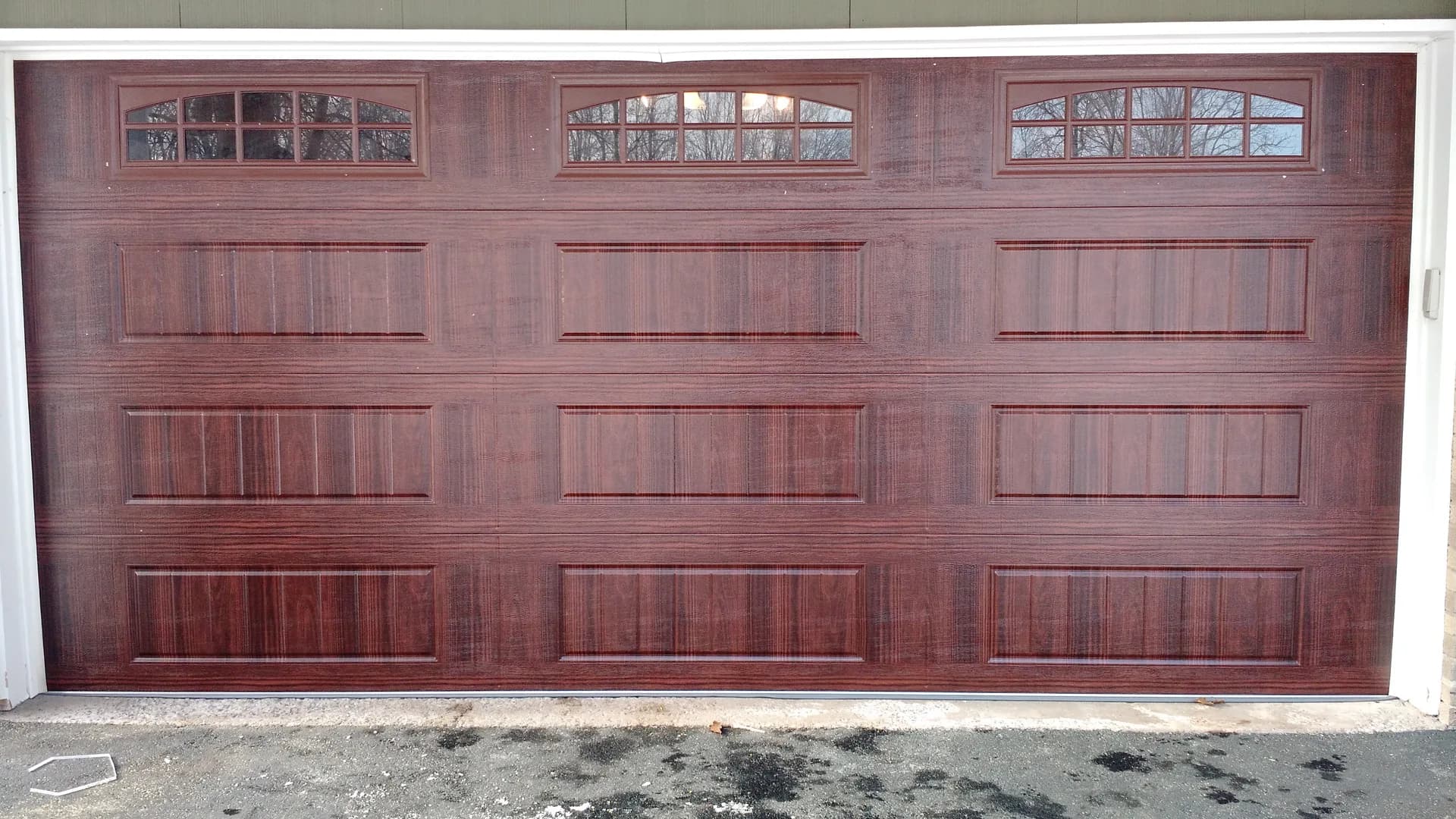 Cherry woodgrain garage door with arched transom windows on a residential home