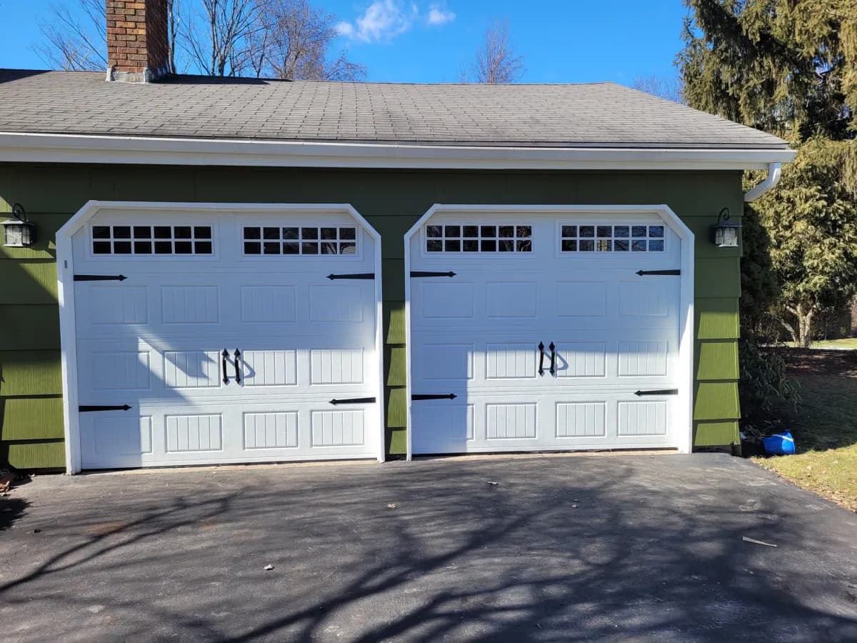 White carriage-style double garage doors on a detached garage with green siding
