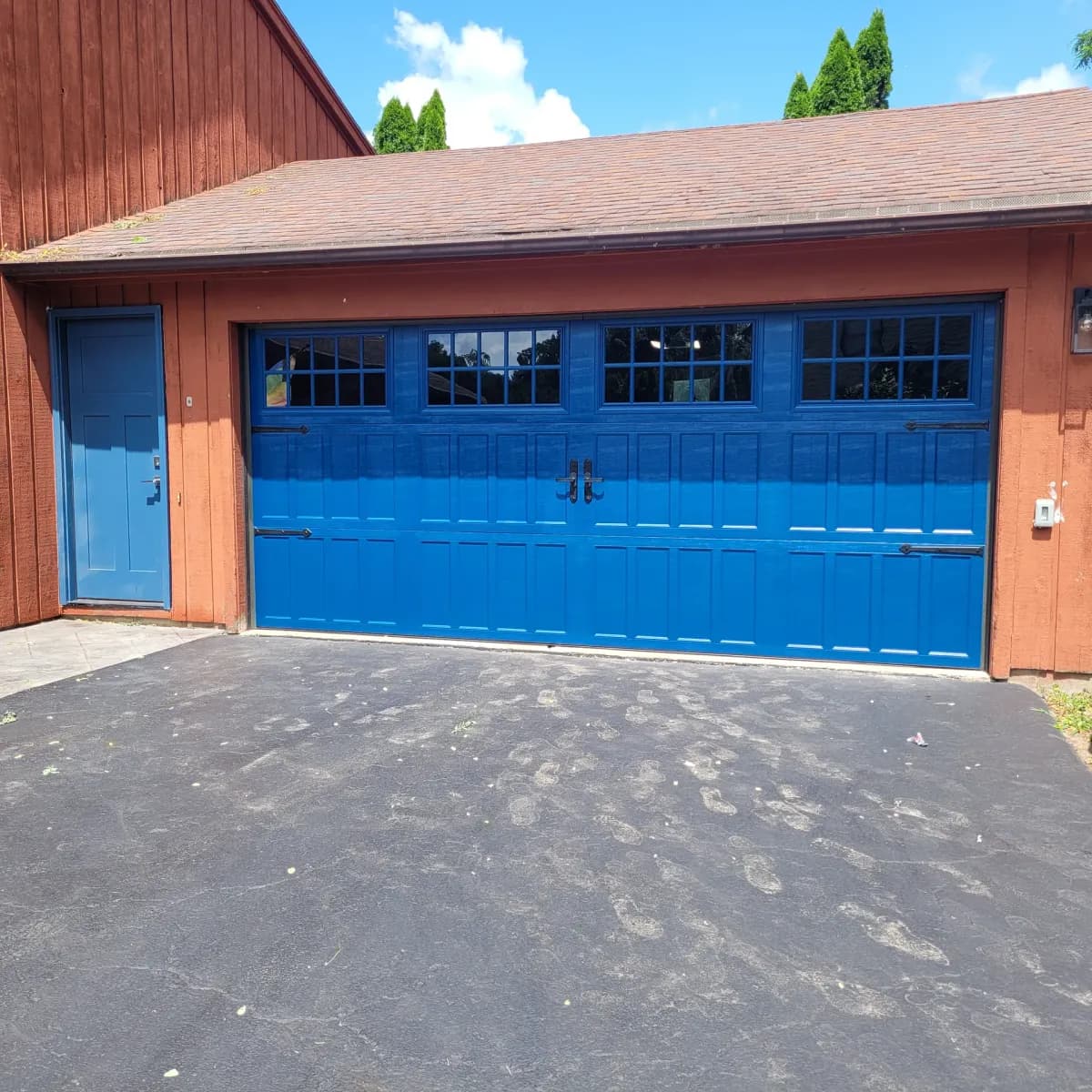 Bold blue carriage-style garage door with grid windows on a brown wood-sided home with matching blue entry door
