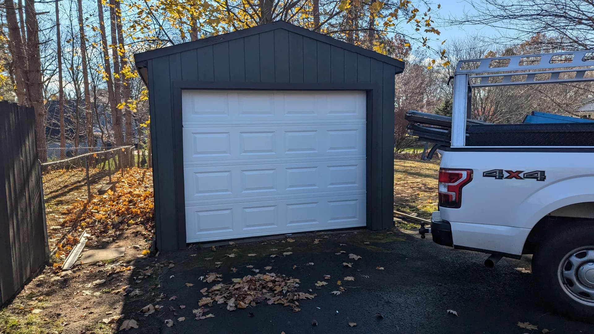 White raised-panel garage door on a charcoal detached garage with autumn leaves