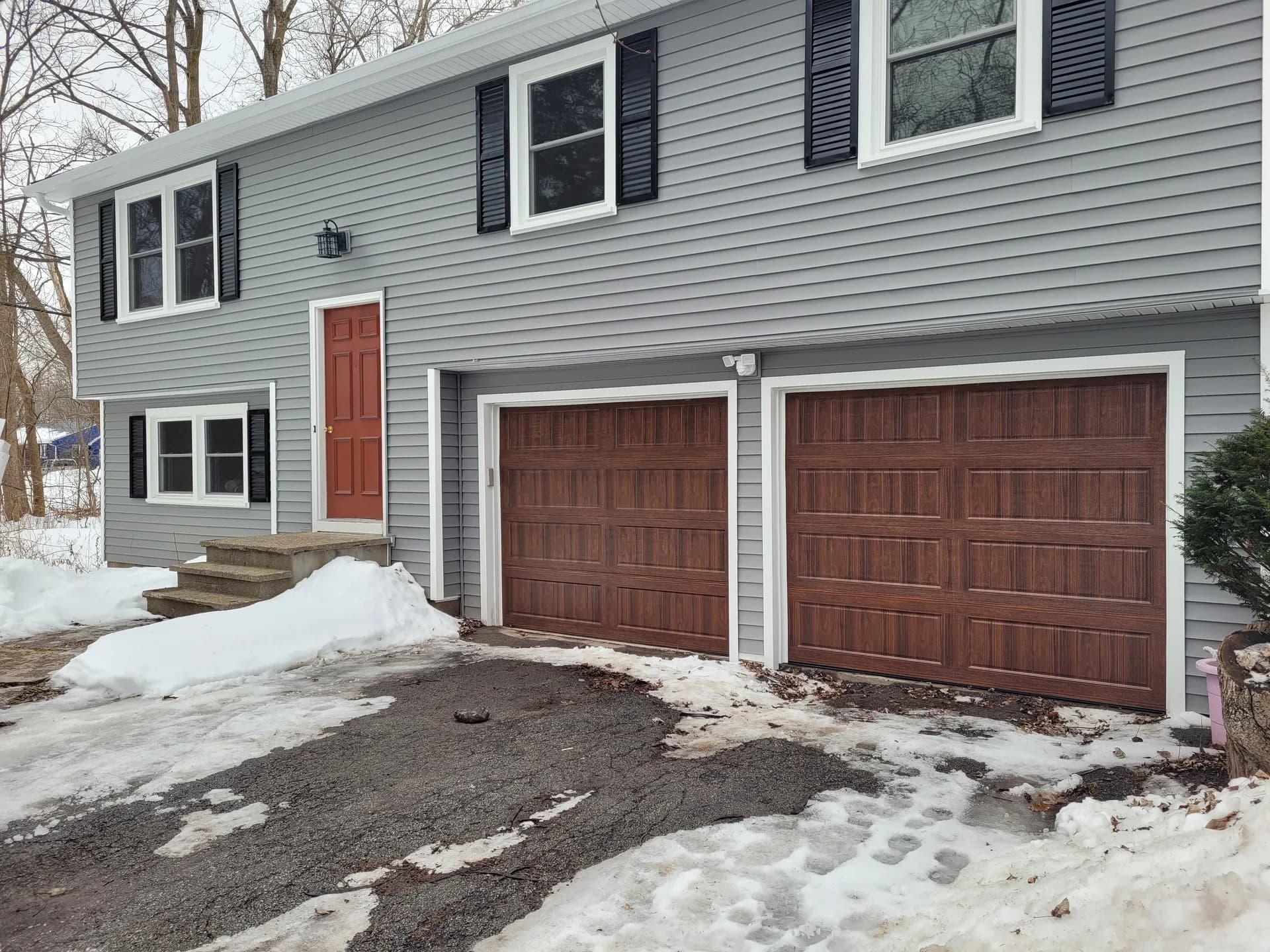 Pair of walnut woodgrain garage doors on a gray colonial home with black shutters