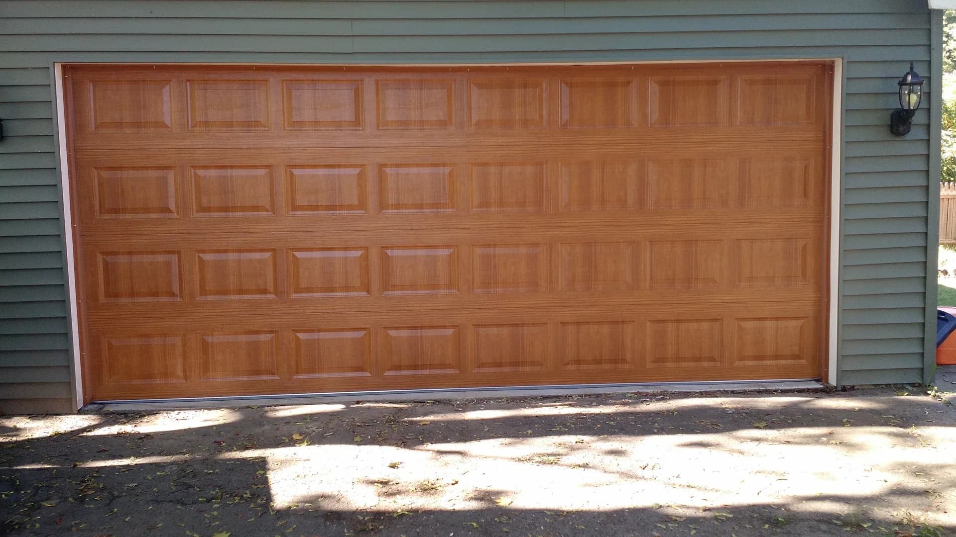 Golden oak raised-panel garage door on a home with green siding